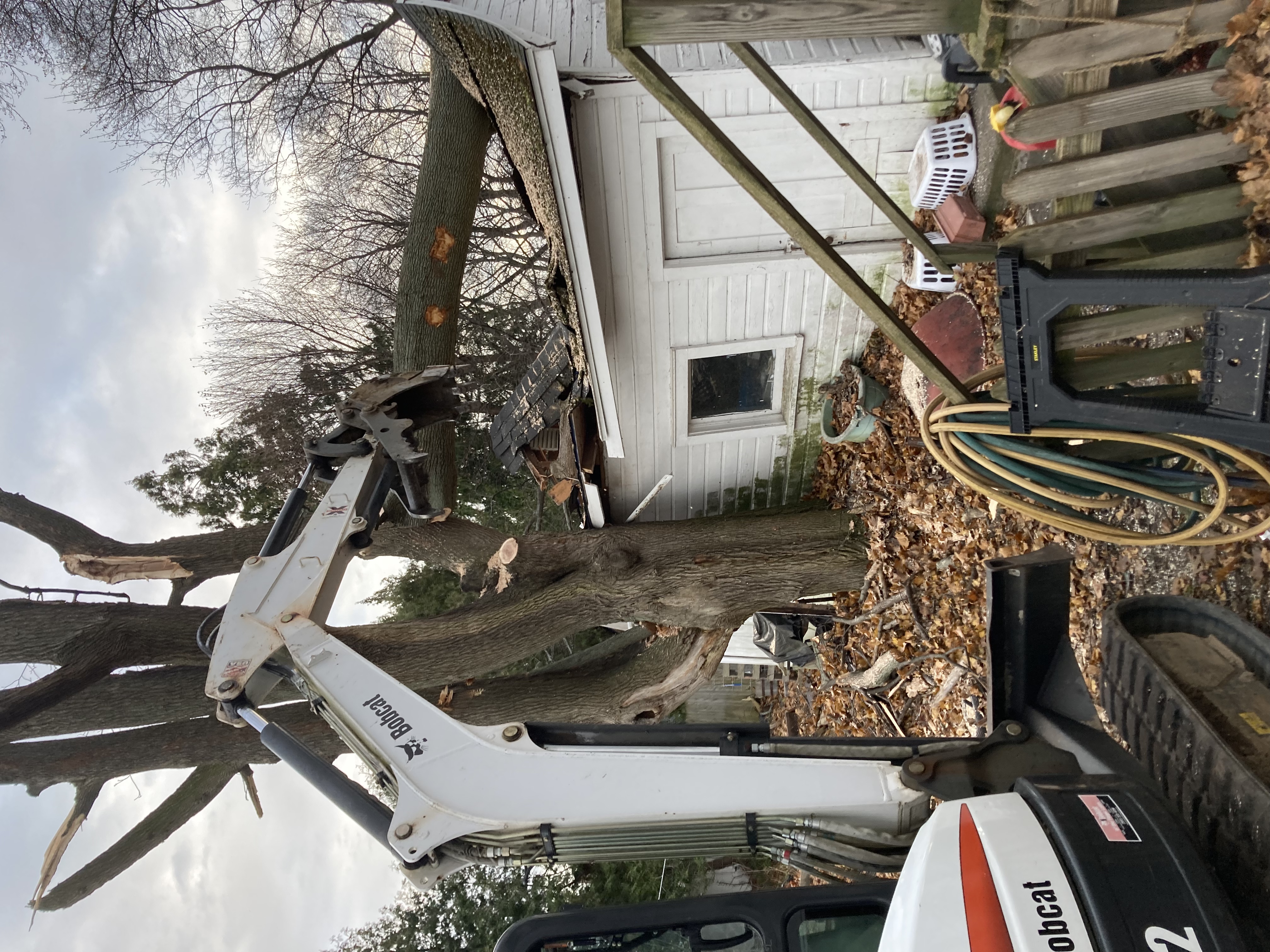 Tracked excavator carefully removing a fallen storm tree from a structure